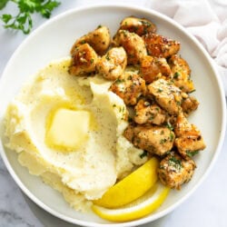 Chicken Bites on a white plate next to mashed potatoes and lemon wedges.