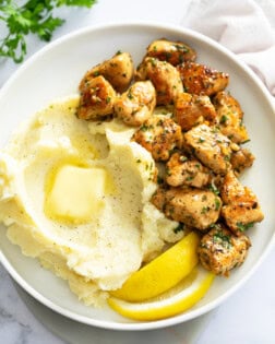 Chicken Bites on a white plate next to mashed potatoes and lemon wedges.