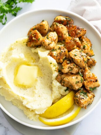 Chicken Bites on a white plate next to mashed potatoes and lemon wedges.