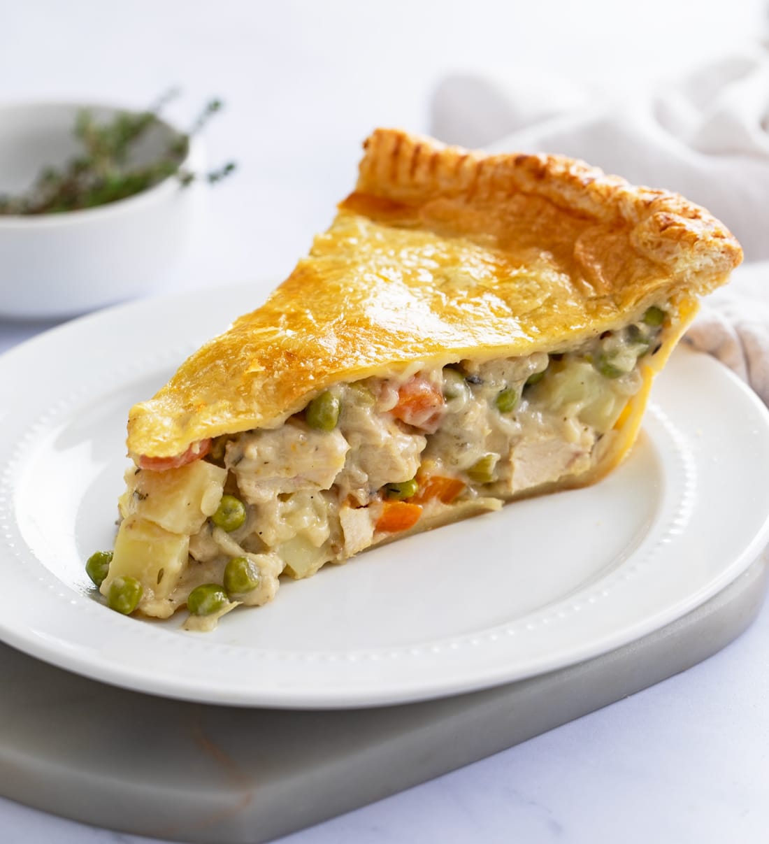 A slice of Chicken Pot Pie with a flaky puff pastry crust and thick filling on a white plate.