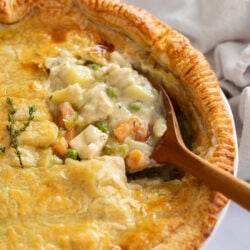 A wooden spoon scooping up Chicken Pot Pie filling from a pie with a flaky puff pastry crust.