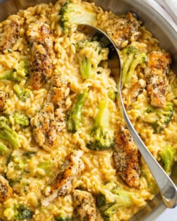 Chicken and Orzo in a skillet with a creamy cheese sauce and broccoli with a spoon on the side.