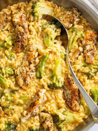 Chicken and Orzo in a skillet with a creamy cheese sauce and broccoli with a spoon on the side.