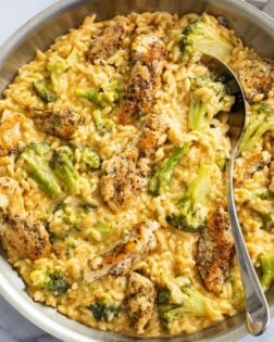 Chicken and Orzo in a creamy cheese sauce with broccoli in a skillet with a spoon on the side.