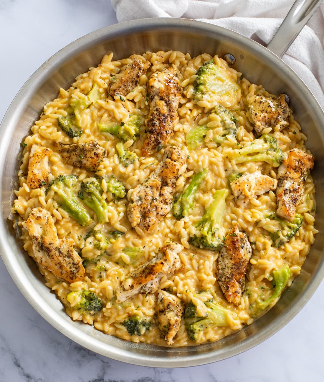 A skillet of Chicken and Orzo with Broccoli in a creamy cheese sauce.