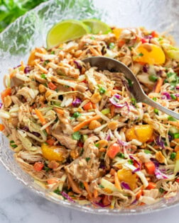 Thai Chicken Salad in a glass bowl with a spoon scooping it up.