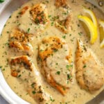 Garlic Parmesan Chicken in a skillet with sauce, fresh parsley, and lemon wedges on the side.