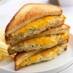 Slices of Tuna Melts stacked on top of each other on a white plate with melted cheese and grilled bread.
