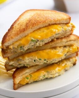 Slices of Tuna Melts stacked on top of each other on a white plate with melted cheese and grilled bread.