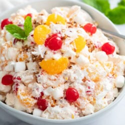 Creamy Ambrosia Salad in a white bowl with cherries and mandarin oranges on top.