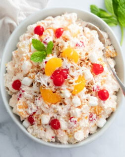 Overhead view of a creamy Ambrosia Salad in a white bowl with cherries and mandarin oranges on top.