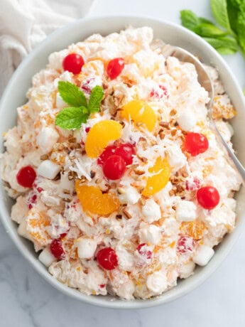 Overhead view of a creamy Ambrosia Salad in a white bowl with cherries and mandarin oranges on top.