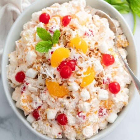Overhead view of a creamy Ambrosia Salad in a white bowl with cherries and mandarin oranges on top.