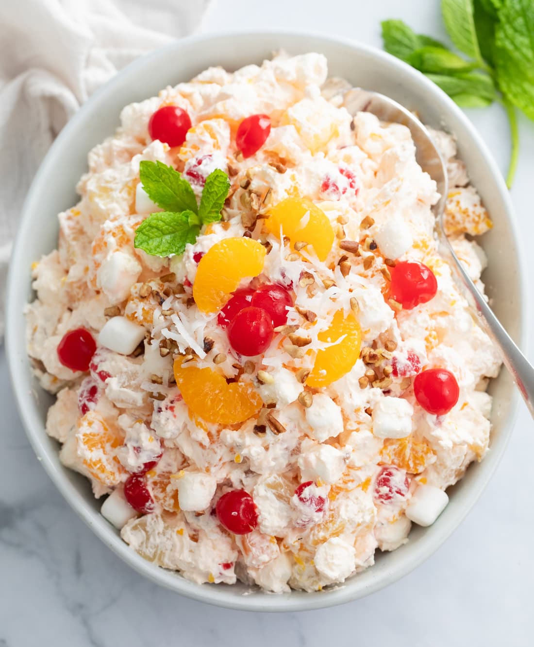 Ambrosia Salad in a white bowl with cherries, mandarin oranges, and fresh mint on top.