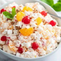 Creamy Ambrosia Salad in a white bowl with cherries and mandarin oranges on top.