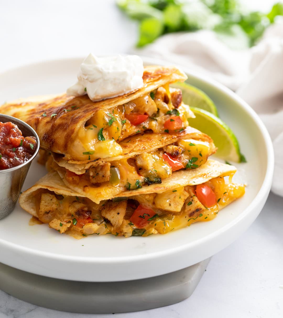 A stack of Chicken Quesadillas with a dollop of sour cream on top and salsa on the side.