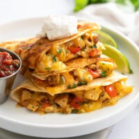 A stack of Chicken Quesadillas on a white plate with a dollop of sour cream on top.