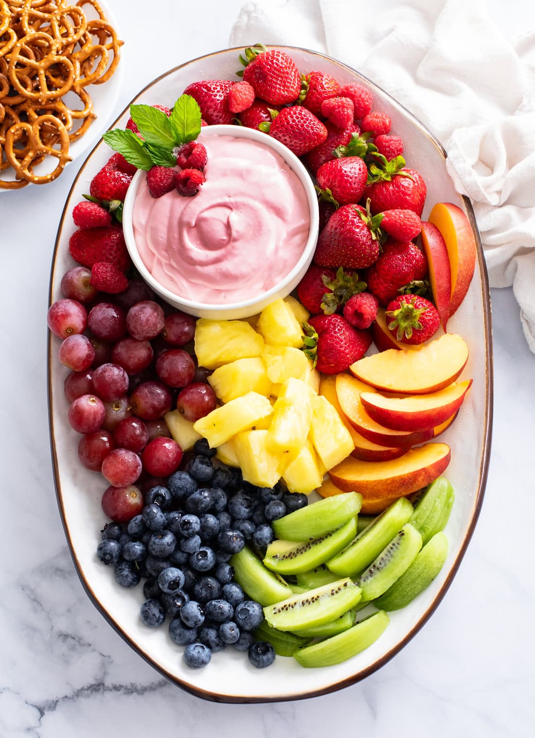 Overhead view of a big colorful platter of fruit with a bowl of fruit dip on the side.