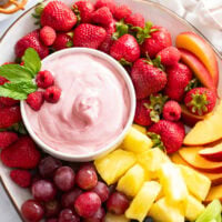 Fruit Dip in a white bowl on a platter with colorful fruit and a garnish of mint and raspberries.