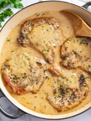 Garlic Parmesan Pork Chops in a skillet with a spoon on the side and parsley on top.