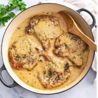Garlic Parmesan Pork Chops in a skillet with sauce and a wooden spoon on the side.