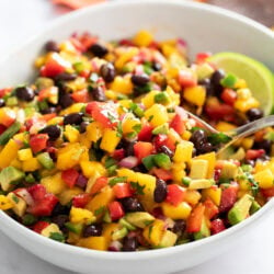 Mango Salsa in a white bowl with a spoon scooping it up.