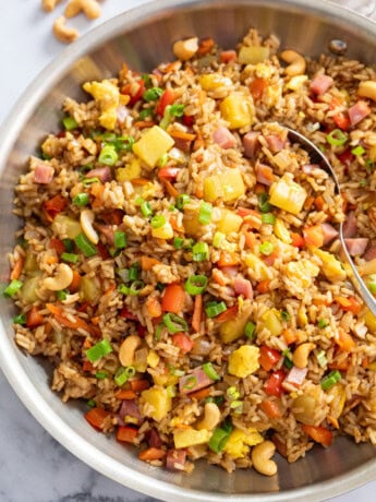 A skillet of Pineapple Fried Rice topped with green onions and cashews.