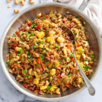 Pineapple Fried Rice in a stainless steel skillet with a silver spoon on the side.