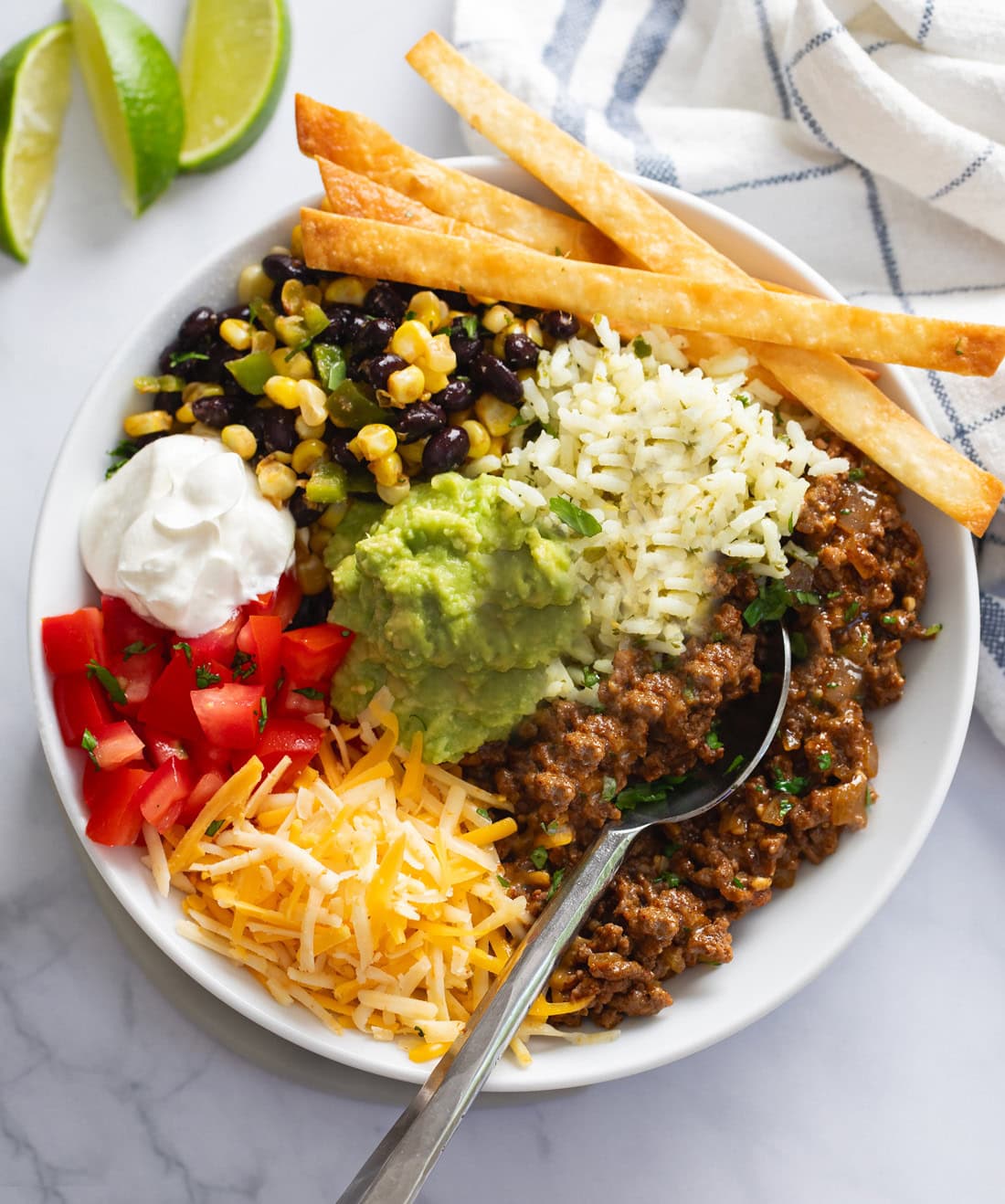 A Burrito Bowl with seasoned ground beef, cilantro lime rice, black beans, corn, cheese, guacamole, and tomatoes.