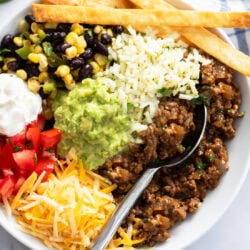 Close up view of the ingredients of a Burrito Bowl, including ground beef, guacamole, rice, beans, corn, tomatoes, cheese, and sour cream.