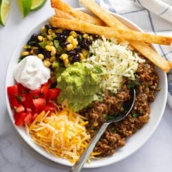 Burrito Bowls filled with rice, seasoned ground beef, corn, black beans, tomatoes, sour cream, and fried tortilla strips.