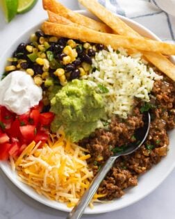 Burrito Bowls filled with rice, seasoned ground beef, corn, black beans, tomatoes, sour cream, and fried tortilla strips.