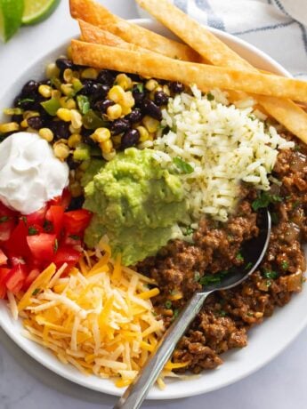 Burrito Bowls filled with rice, seasoned ground beef, corn, black beans, tomatoes, sour cream, and fried tortilla strips.