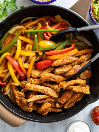 Chicken Fajitas in a skillet with multi-colored bell peppers and strips of seasoned chicken.