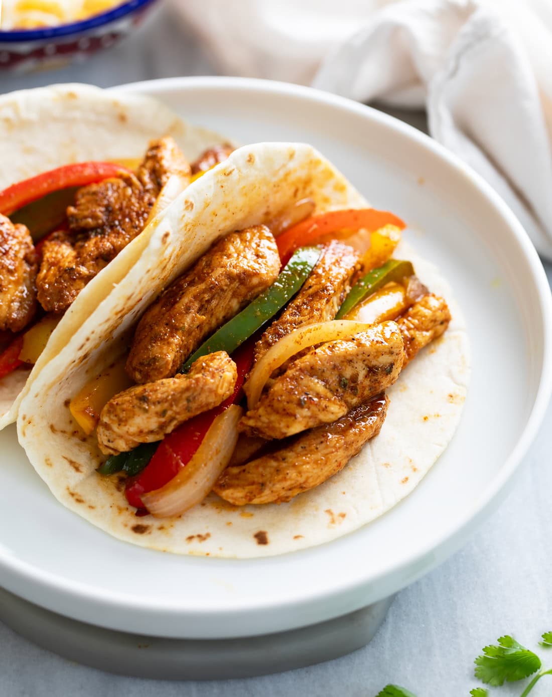 Chicken Fajitas with chicken, onions, and peppers in a tortilla on a white plate.