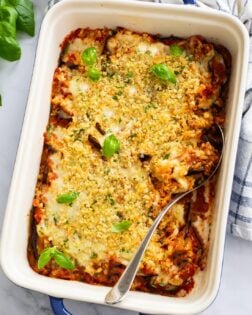A casserole dish filled with Eggplant Casserole with breadcrumbs and fresh basil on top.
