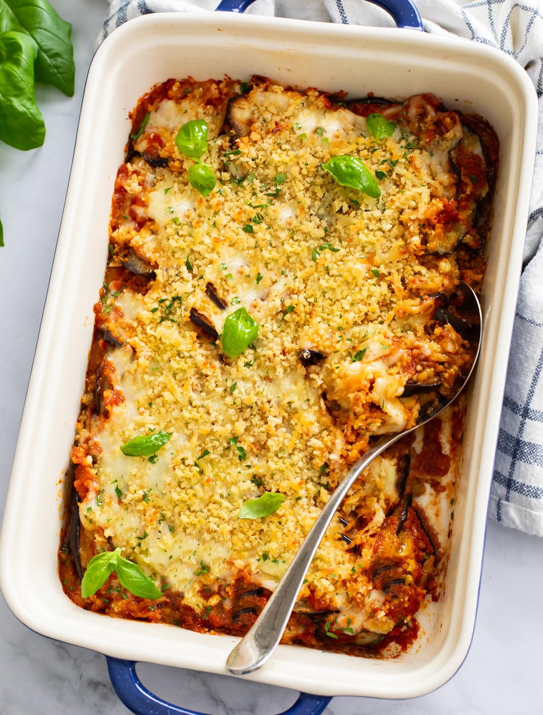 A casserole dish filled with Eggplant Casserole with breadcrumbs and fresh basil on top.