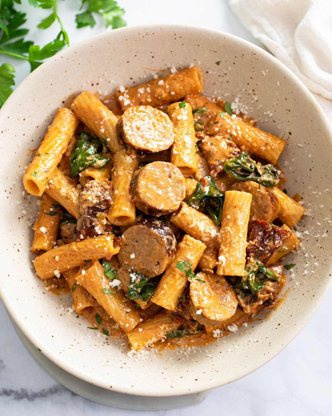 A bowl filled with Sundried Tomato Pasta with slices of sausage and a tomato cream sauce.