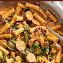 A labeled picture of Sun-Dried Tomato Pasta in a skillet with spinach and sausage.