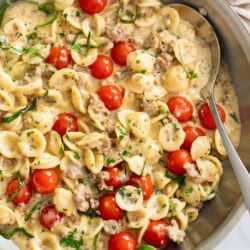 Tomato Basil Pasta in a skillet with fresh tomatoes and basil in a cream sauce with a spoon on the side.