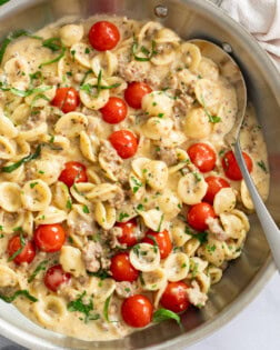 Tomato Basil Pasta in a skillet with fresh tomatoes and basil in a cream sauce with a spoon on the side.