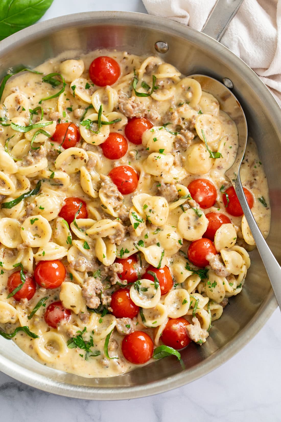 Tomato Basil Pasta in a skillet with fresh tomatoes and basil in a cream sauce with a spoon on the side.