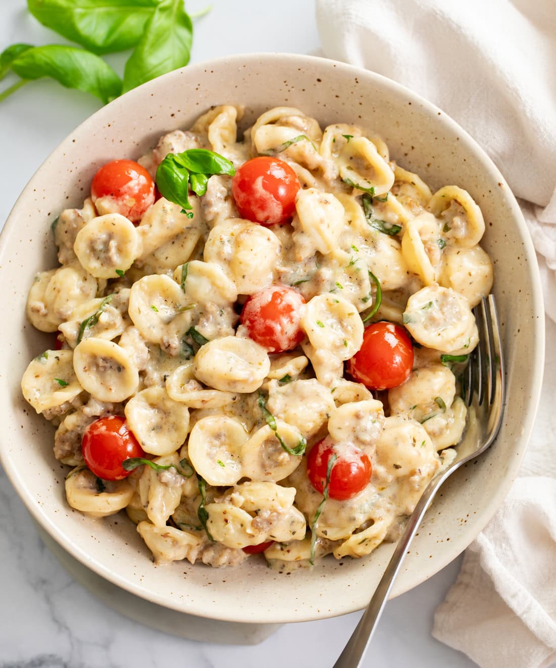 A bowl filled with Tomato Basil Pasta in a creamy sauce with a fork on the side.