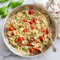 A skillet of Tomato Basil Pasta in a creamy sauce with a spoon on the side.