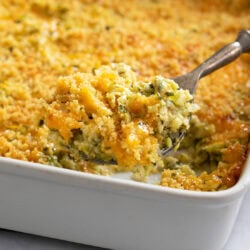 A casserole dish filled with Zucchini Casserole with a spoon scooping it out.