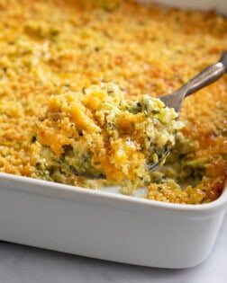 A casserole dish filled with Zucchini Casserole with a spoon scooping it out.