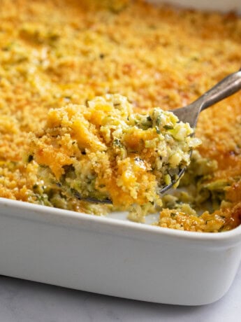 A casserole dish filled with Zucchini Casserole with a spoon scooping it out.