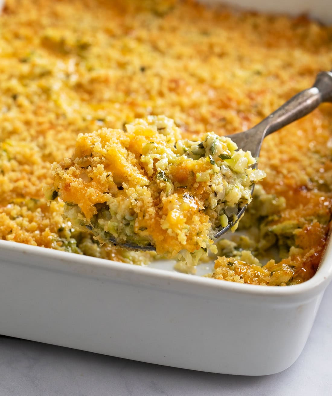 A casserole dish filled with Zucchini Casserole with a spoon scooping it out.