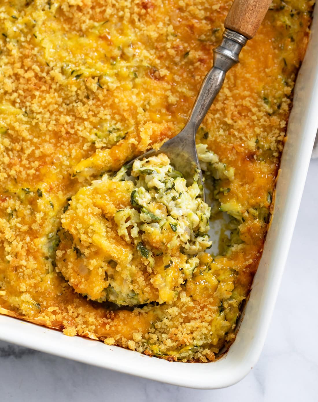 A spoon in a casserole dish of Zucchini Casserole.