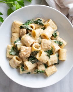 Chicken Spinach Pasta in creamy sauce in a white bowl with Mezza rigatoni pasta.